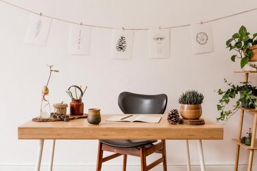 Stylish scandinavian home interior of open space, with a lot of plants, design accessories, bamboo shelf, wooden desk and hanging mock up forest drawings. 