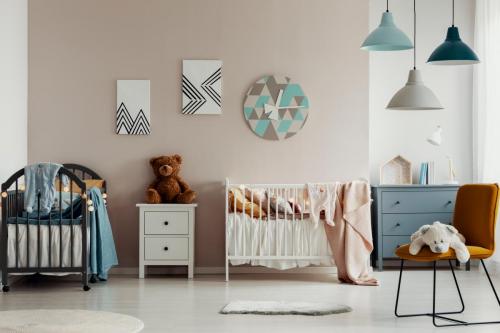 Chic baby bedroom with wooden cribs, lamps, white wooden nightstand with brown teddy bear and fashionable yellow chair